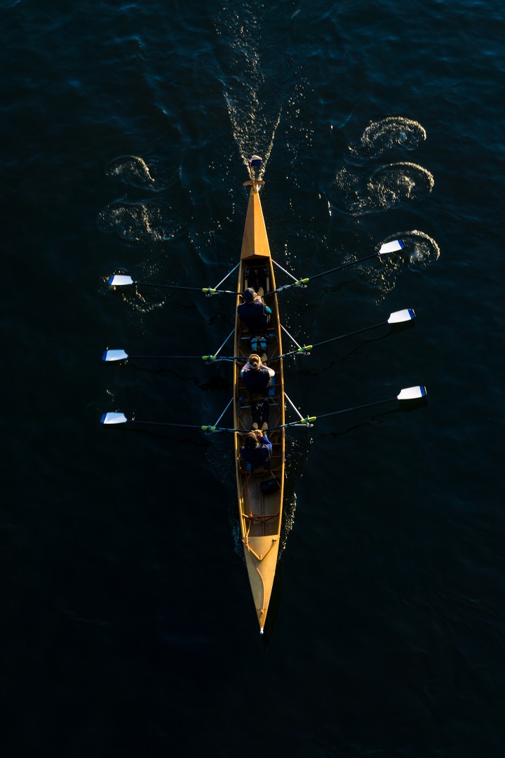 Close-up of a powerful Rowing Team in a Rowing Boat.
View from above of a floating Rowing Boat with three Canoeists on a River.